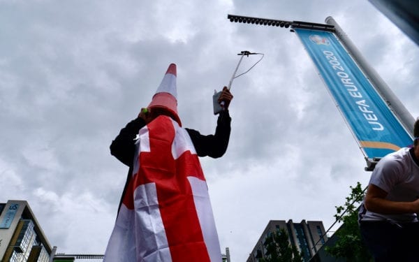 An England fan with a traffic cone on his head and draped in an England flag stands above the crowd outside Wembley Stadium.