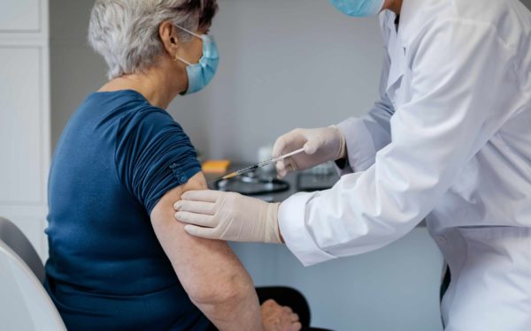Older woman being given a vaccine booster by a female doctor.