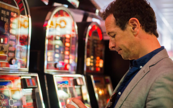 Man gambling in casino with fruit machines losing money, invest don't gamble