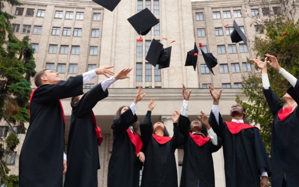 International group of students standing in a row and throwing graduation caps up in the air