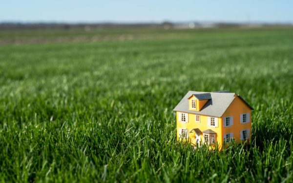 Little toy model yellow house in he middle of large grass meadow field. Horizon line and sky. Miniature, scale, downsize, mortgage payment, big yard, tiny, small,