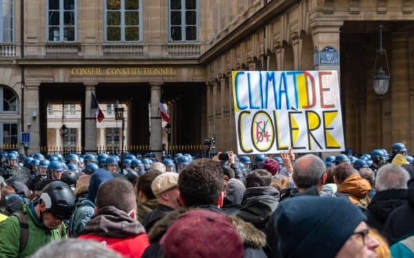 French protesters against Macron's retirement reform with a sign 'Climate of anger' pass near the Constitutional Council which is examining the law under police (via HJBC/ Shutterstock)