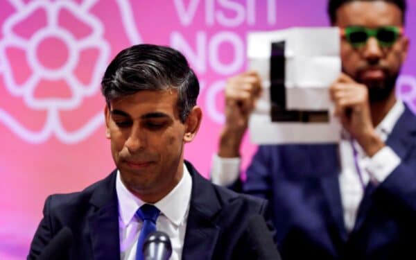 Independent candidate Niko Omilana holds an "L" behind Britain's Prime Minister Rishi Sunak