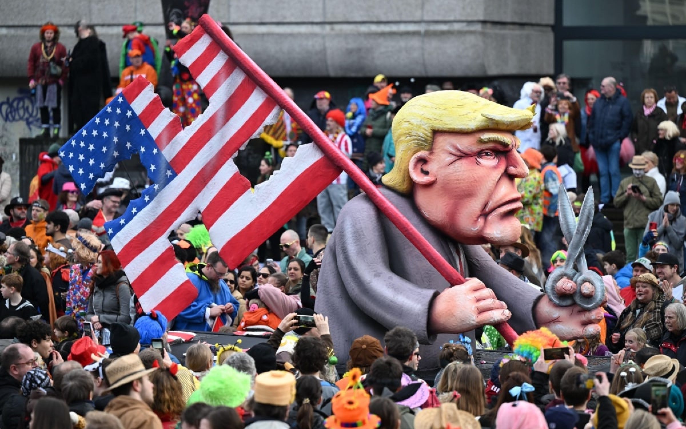 Duesseldorf, Germany. 12th Feb, 2024. The themed float showing US presidential candidate-elect Trump with the US national flag in the shape of a swastika and with a pair of scissors in his hand passes celebrating carnival revellers in the Rose Monday parade. The street carnival reaches its peak on Rose Monday.