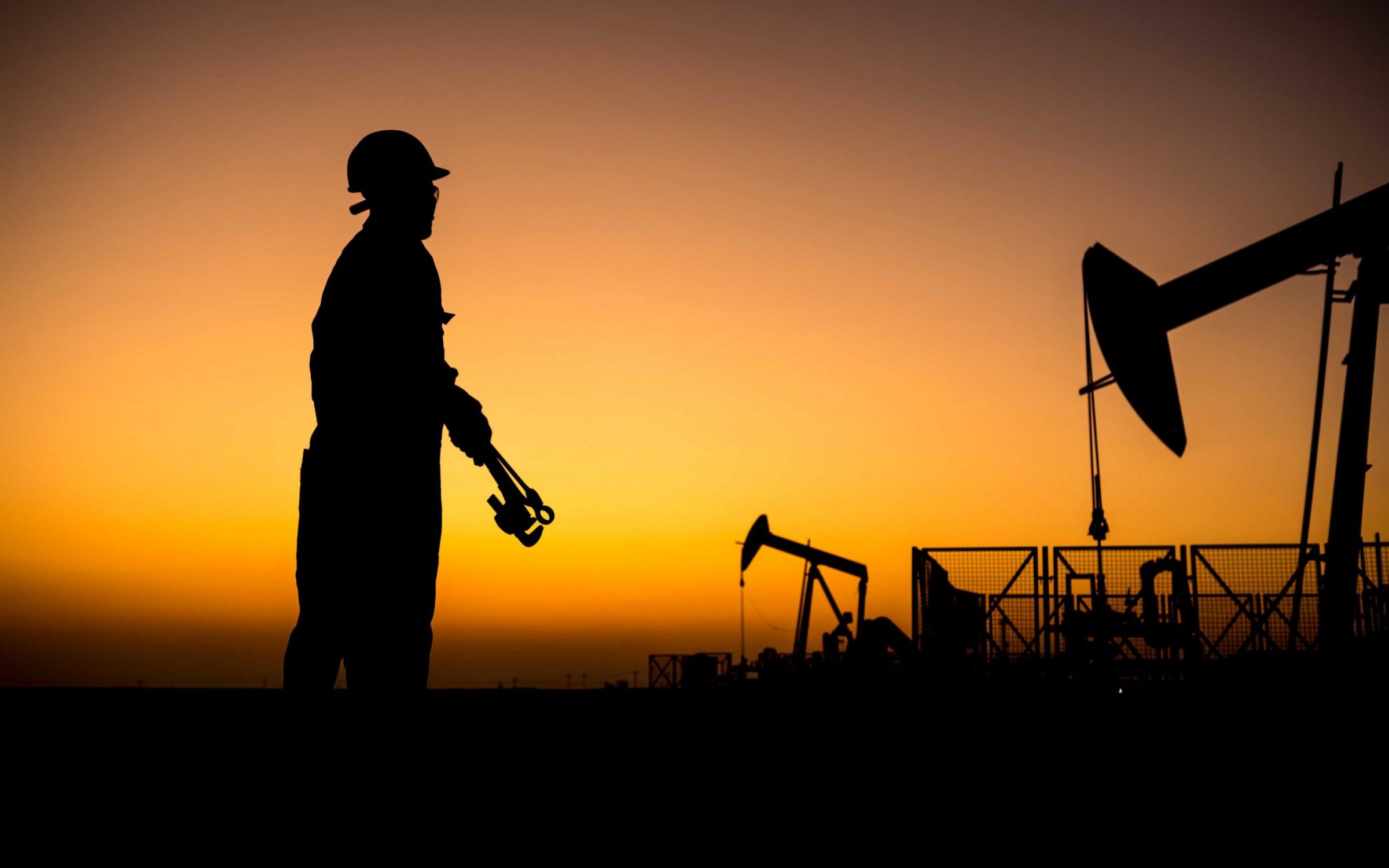 Silhouette of a oilfield worker monitoring crude oil pump at sunset.